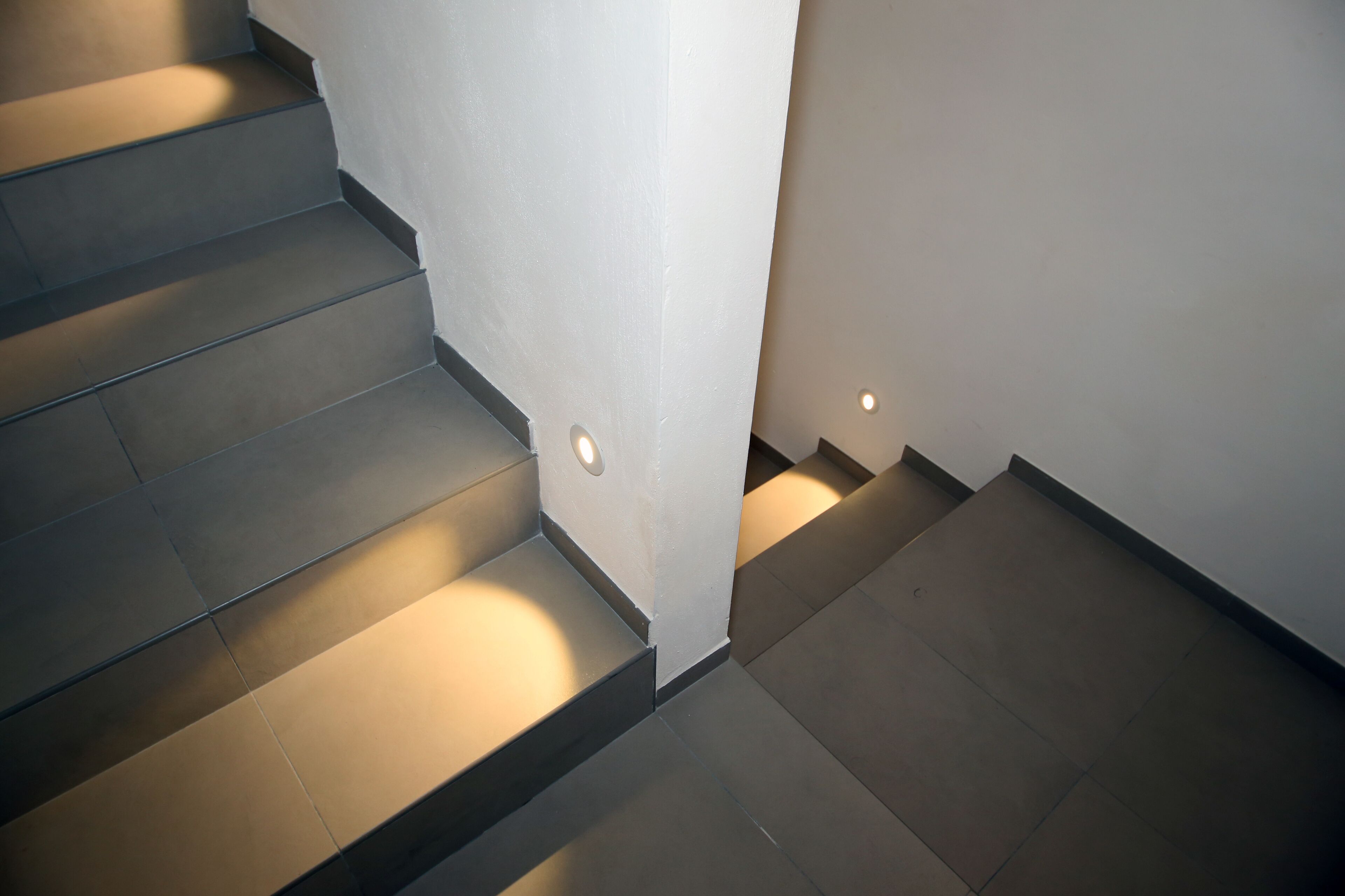 Una escalera moderna de diseño minimalista, con una combinación de pisos oscuros y claros, e iluminación empotrada a lo largo de los peldaños.
