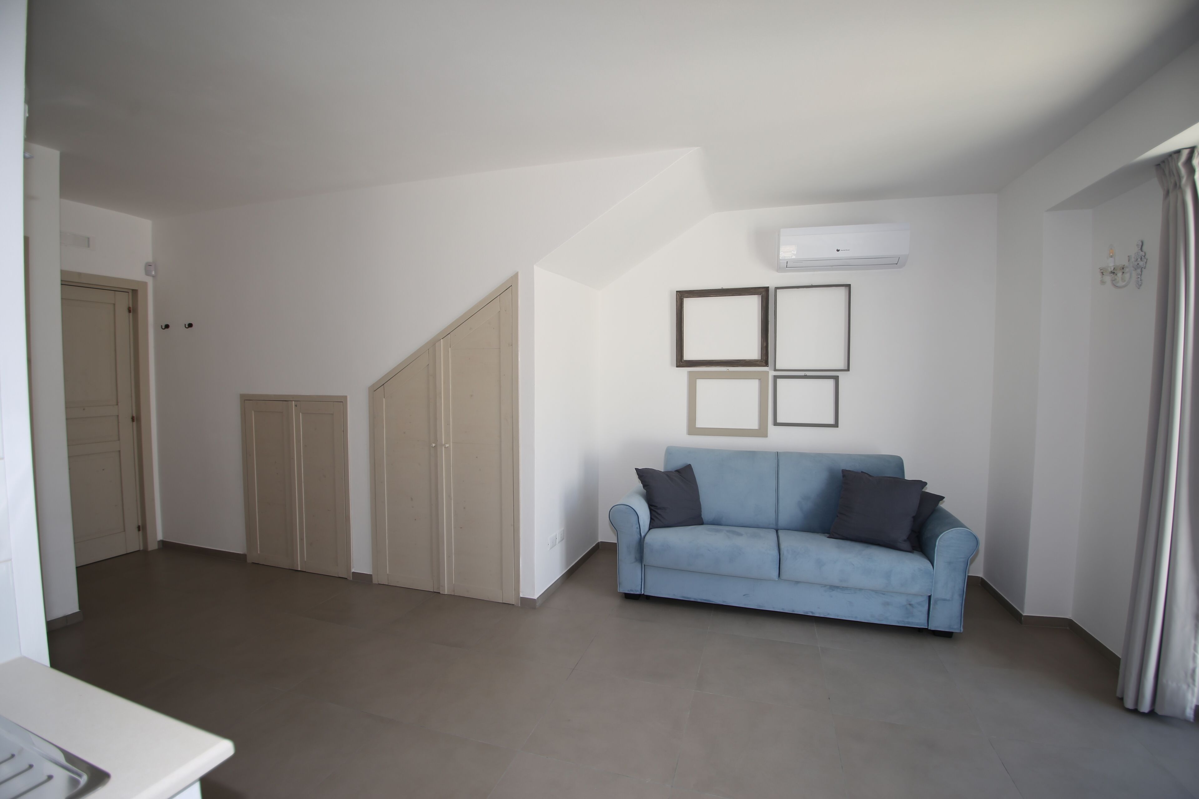 A modern living room with a light blue sofa, a white wall-mounted air conditioner, and a set of closed doors.