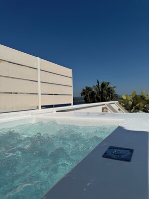 A pool area with clear water, a white deck, and a view of palm trees and the ocean. - Don Alfredo (Taranto)