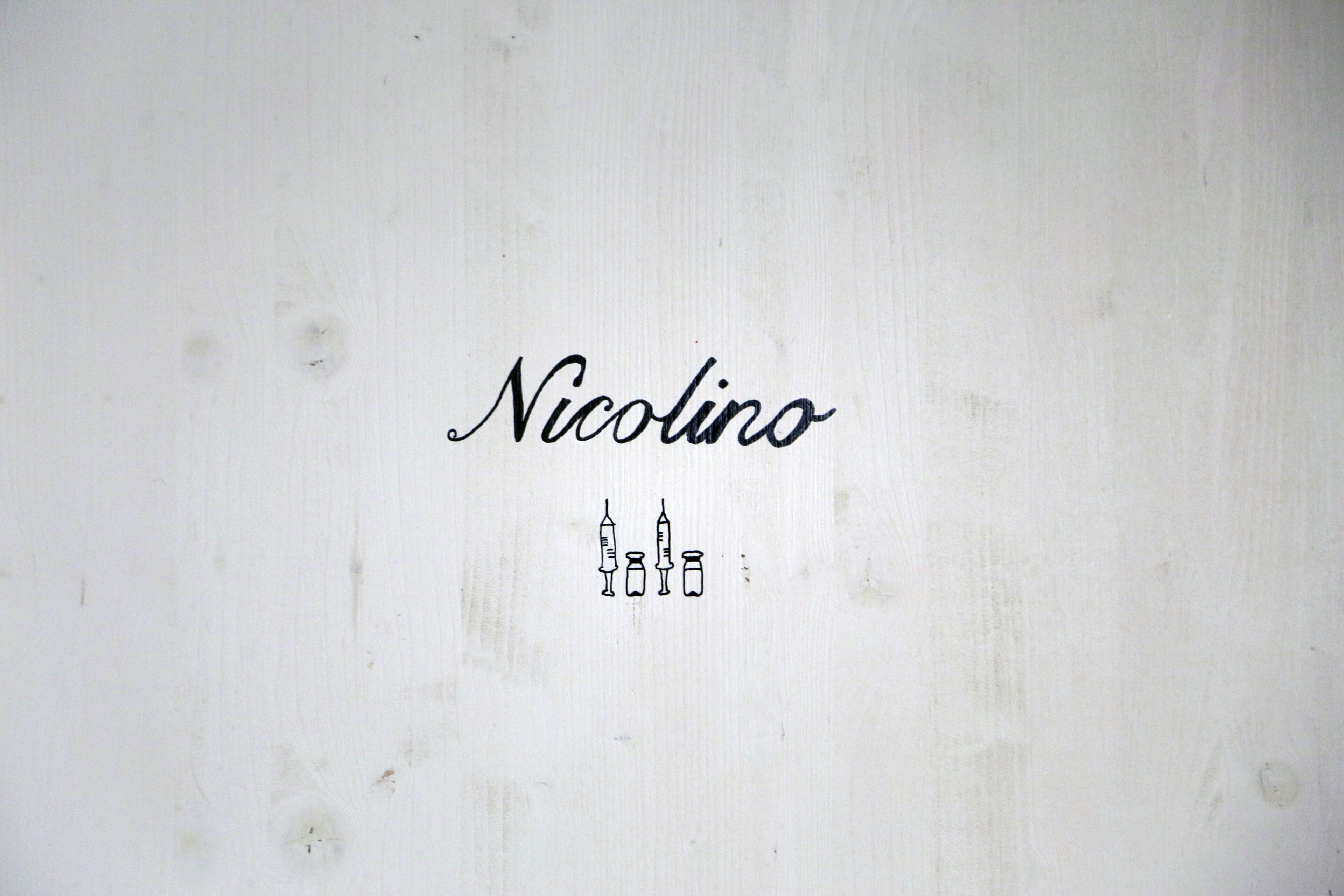 A white wooden wall with the name "Nicolino" and three syringe icons.
