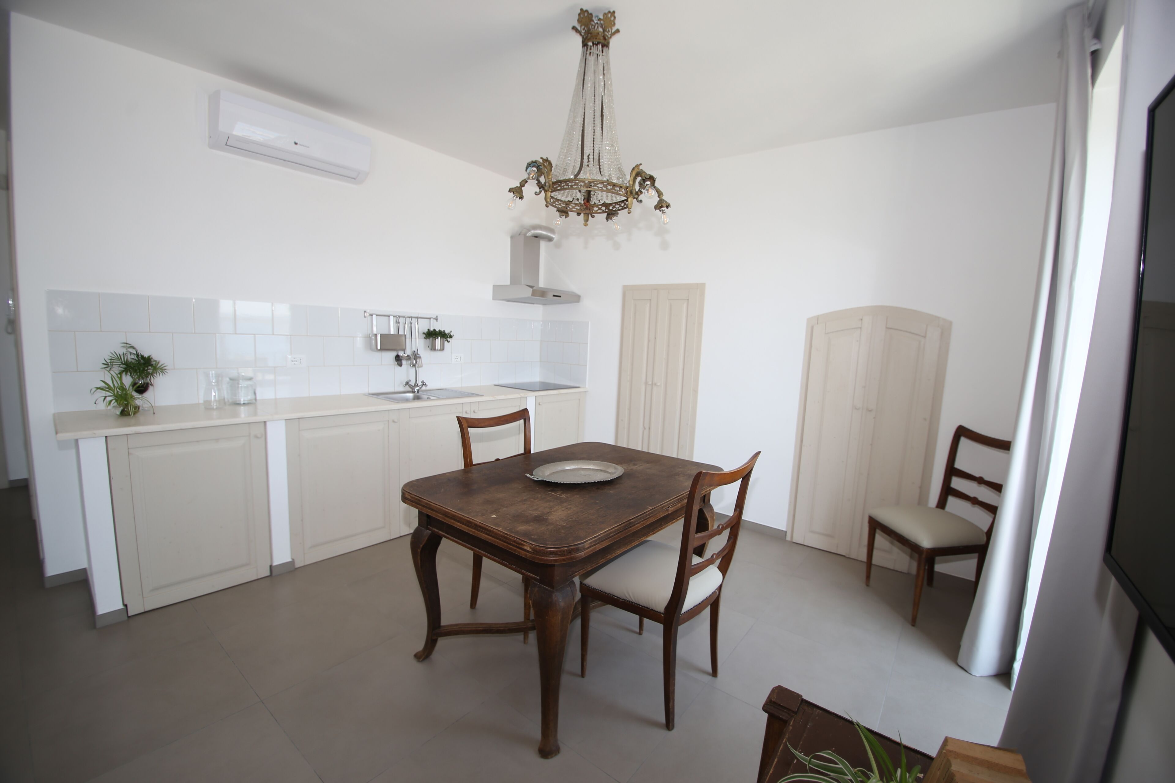 Une cuisine avec une table à manger, des chaises, un lustre et un crédence carrelée de couleur blanche.