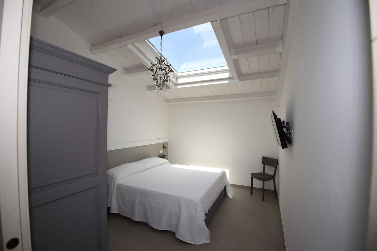 A bedroom with a bed, a chair, a wardrobe, and a skylight.