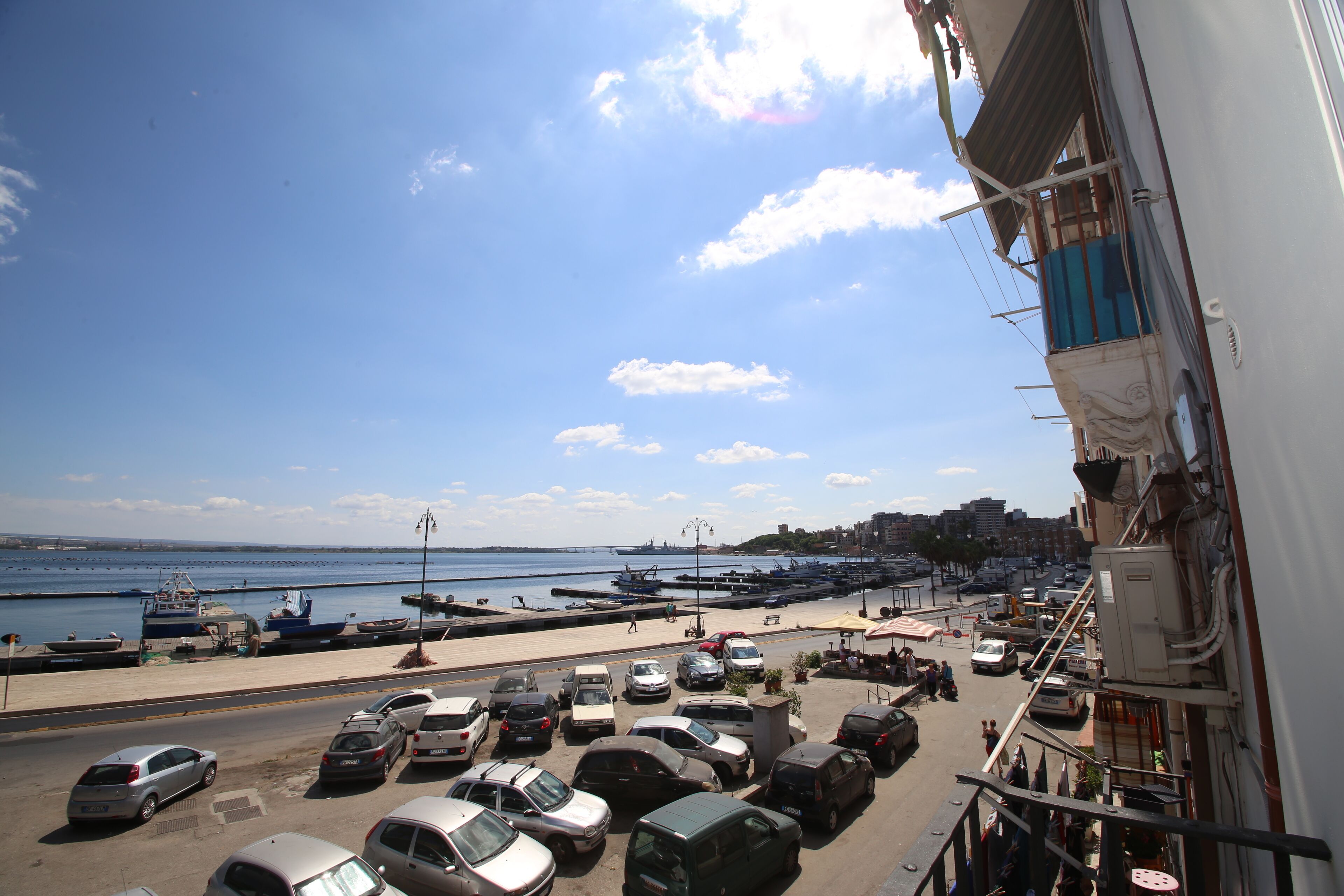 A parking lot with several cars and a view of the sea and boats.