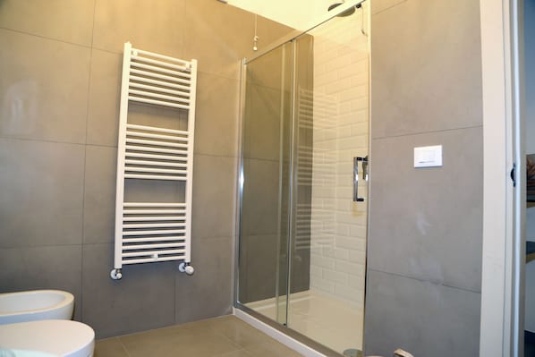 A modern bathroom with a glass shower enclosure, a white towel rack, and a toilet. - Don Alfredo (Taranto)