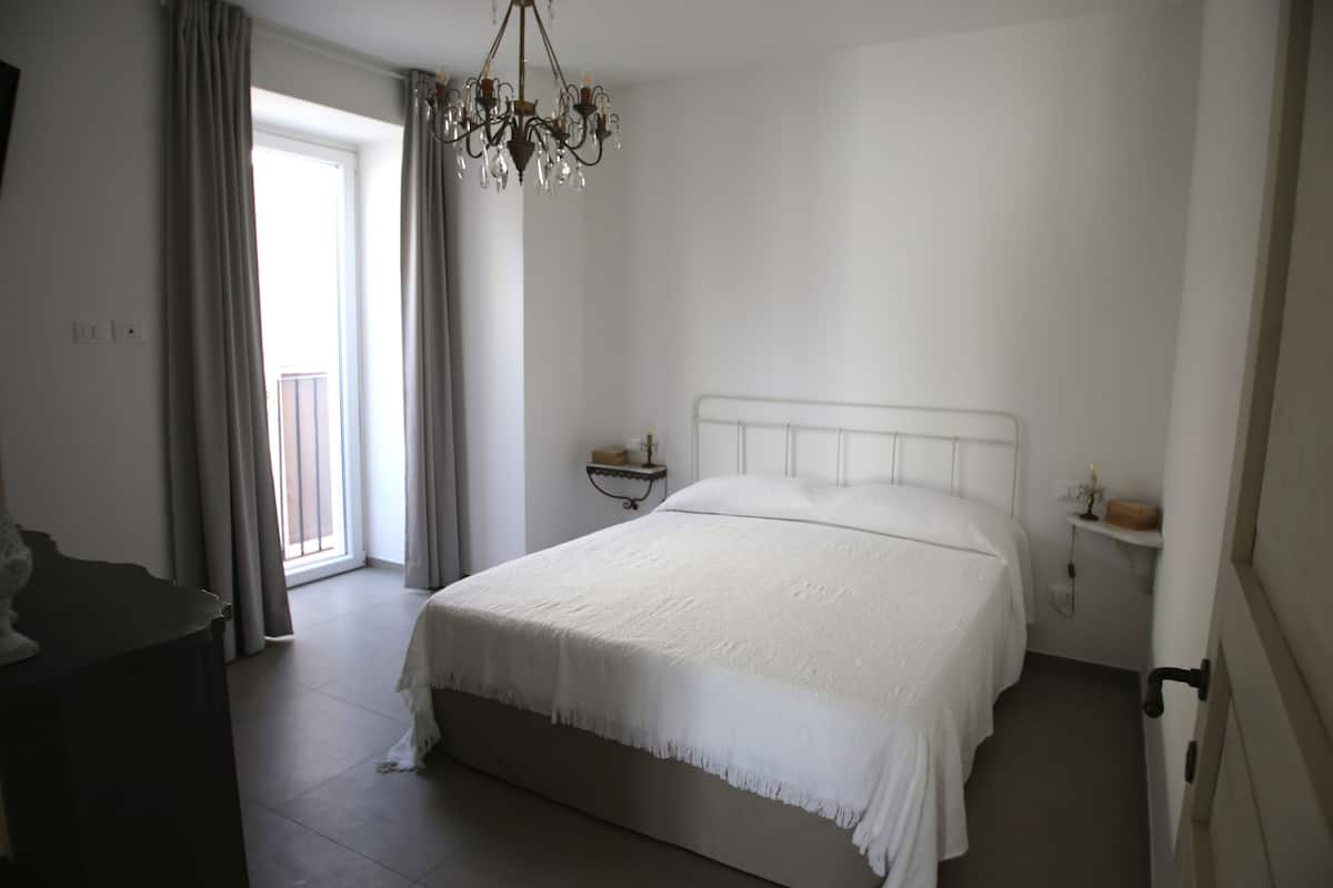 A bedroom with a large bed, a chandelier, a nightstand, and a window with curtains.