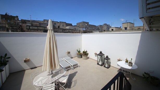 A rooftop terrace with a white table and chairs, a beige umbrella, and potted plants. - Don Alfredo (Taranto)