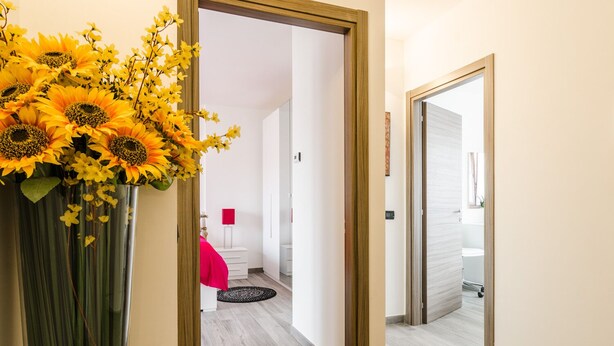 A hallway with a wooden floor, a mirror, and a door leading to a room with a red chair and a small rug.