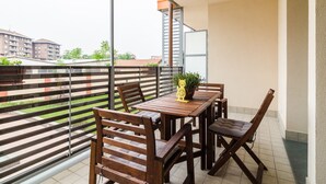 A balcony with a wooden table and chairs, a potted plant, and a yellow cat-shaped decoration.