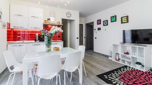 A modern kitchen with white cabinets, a red backsplash, and a dining area with a glass table and white chairs.