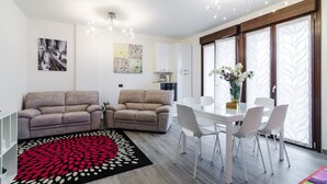 A modern living room with two sofas, a dining table with chairs, and a kitchen area in the background.