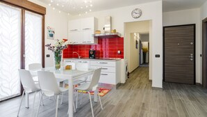 A modern kitchen with white cabinets, a red backsplash, and a dining area with a glass table and white chairs.