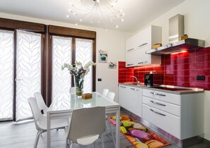 A modern kitchen with white cabinets, a red backsplash, and a glass dining table with chairs.