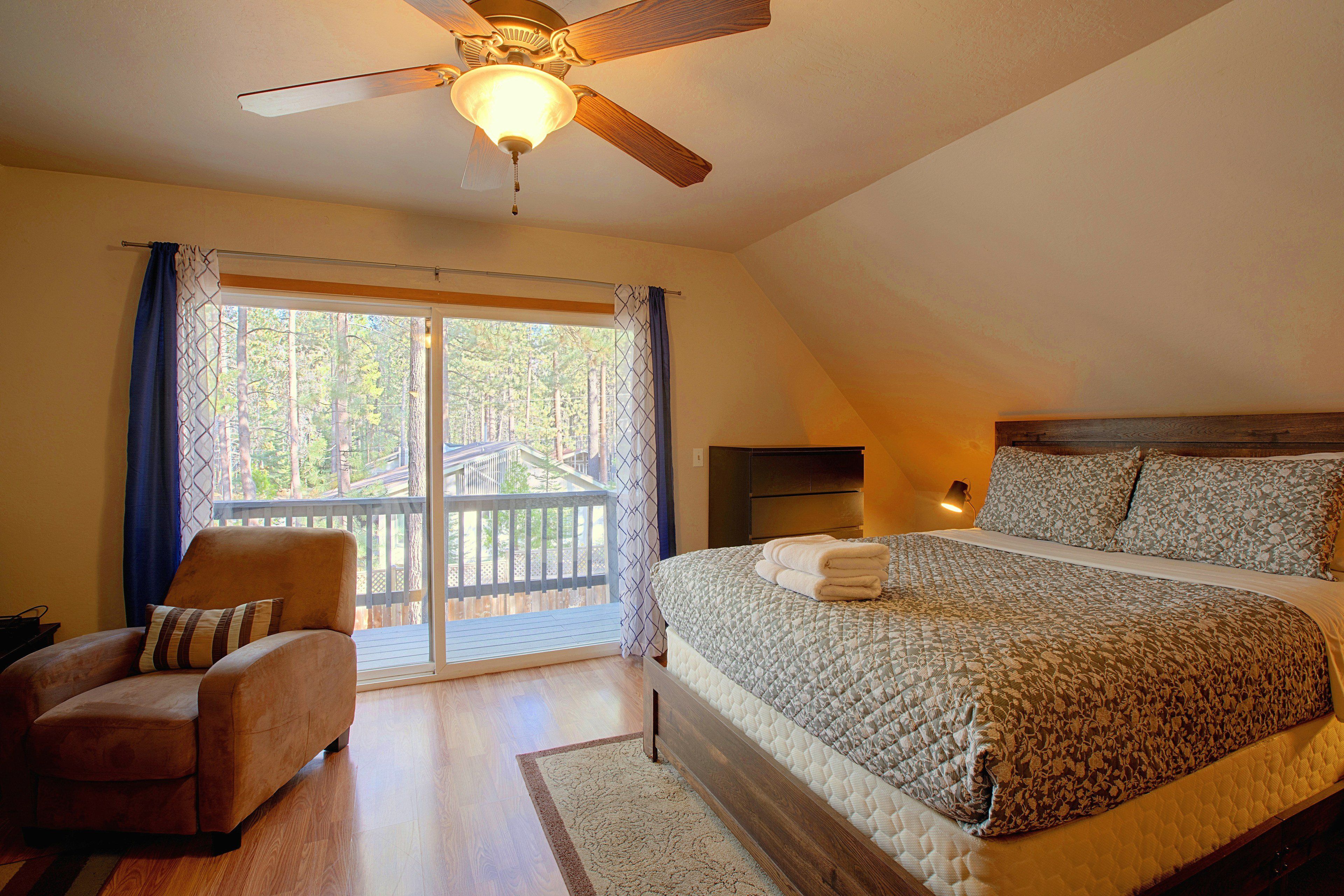 A bedroom with a large bed, a chair, a ceiling fan, and a view of a deck through a sliding door.