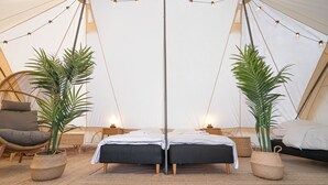 Una carpa con dos camas, luces colgantes y plantas en macetas.