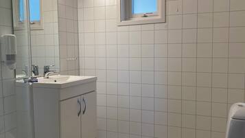 Un baño con azulejos blancos, un lavamanos con espejo, una ventana y un inodoro.