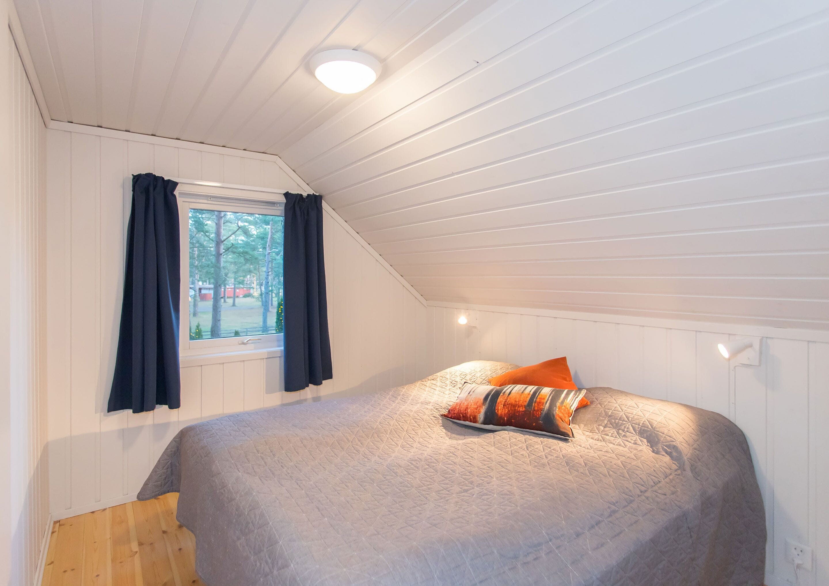 Ein Schlafzimmer mit Bett, Fenster mit Vorhängen und einer Deckenleuchte.