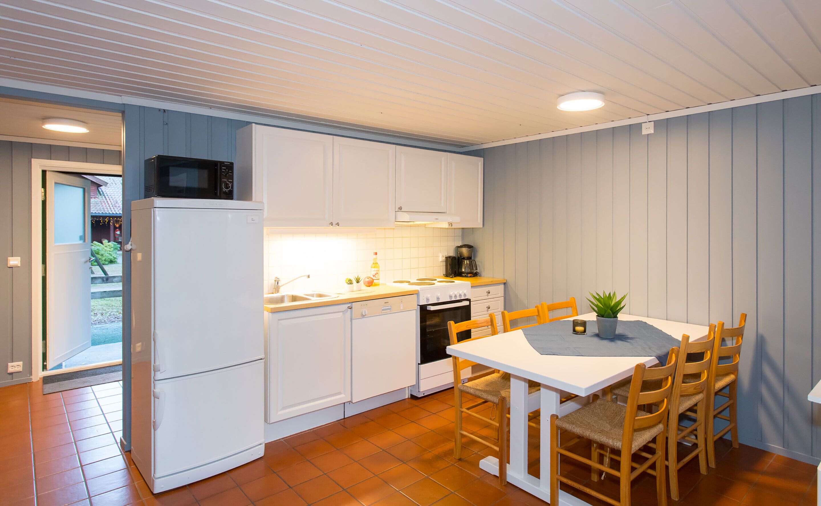 A compact kitchen with white cabinets, a microwave, a stove, and a sink. There's a dining table with chairs and a potted plant.