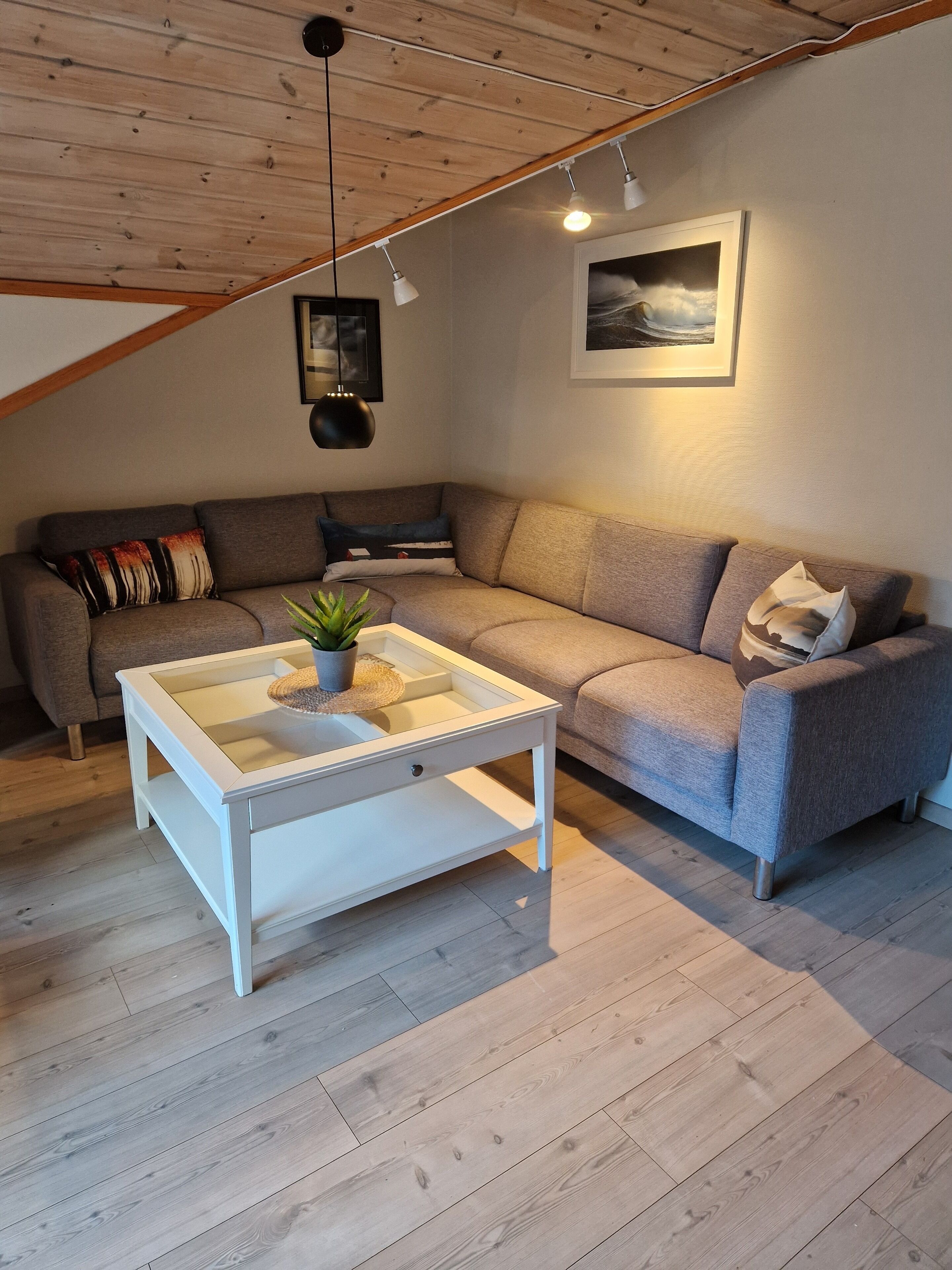 Un salón acogedor con un sofá gris, una mesa de centro blanca y techo de madera.