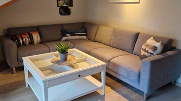 Un salón acogedor con un sofá gris, una mesa de centro blanca y techo de madera.