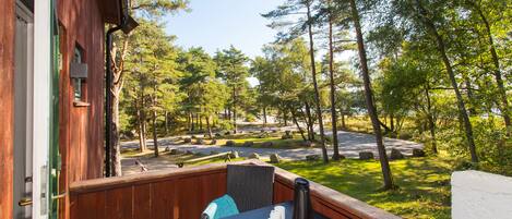 A wooden deck with a table and chairs, overlooking a forested area with a clear sky.
