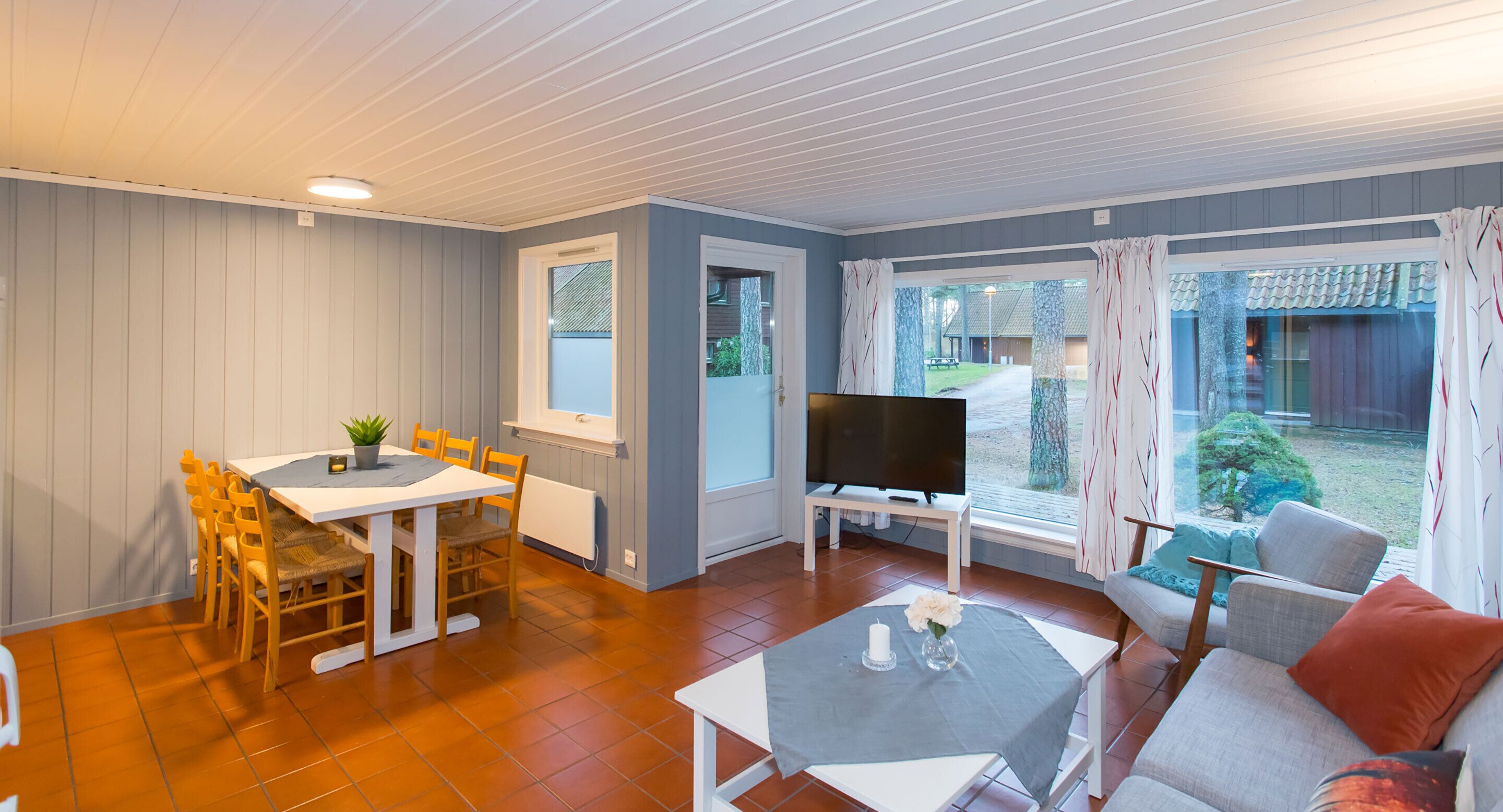 A room with a dining table, chairs, a TV, a sofa, and a window with curtains.