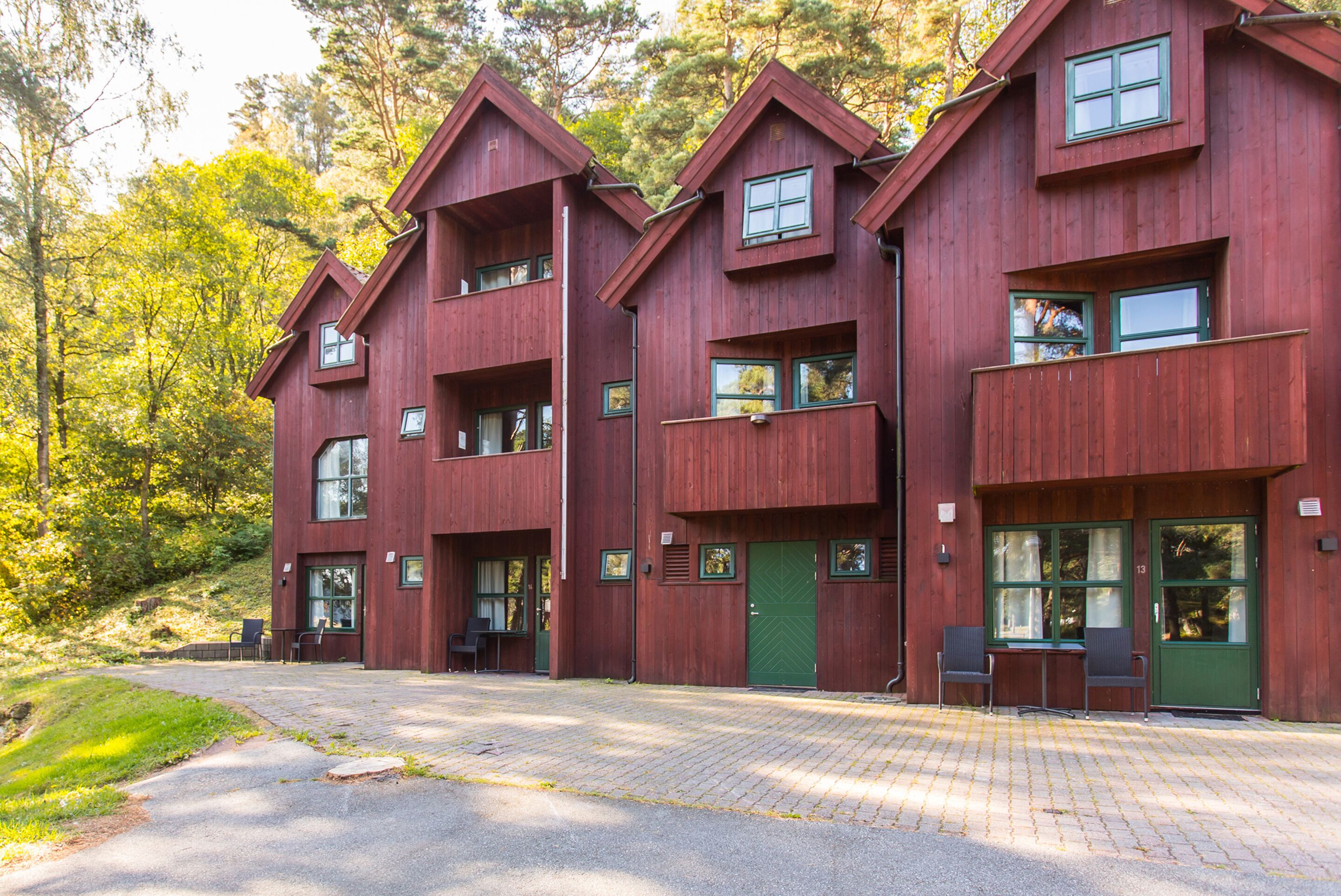 Punainen puinen rakennus, jossa on useita ikkunoita ja ovia, päällystetty sisäänkäynti ja nurmialue, jossa on tuoleja.