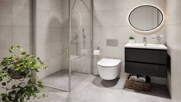 A modern bathroom with a glass-enclosed shower, a white toilet, a black vanity, and a round mirror with a light halo.