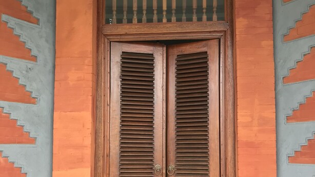 A wooden double door with horizontal slats, set within a decorative wall with geometric patterns.