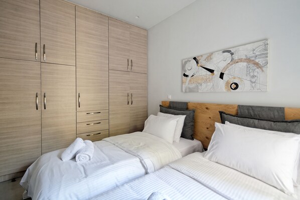 A bedroom with a large wardrobe, a bed with white bedding, and a wall-mounted abstract art piece.