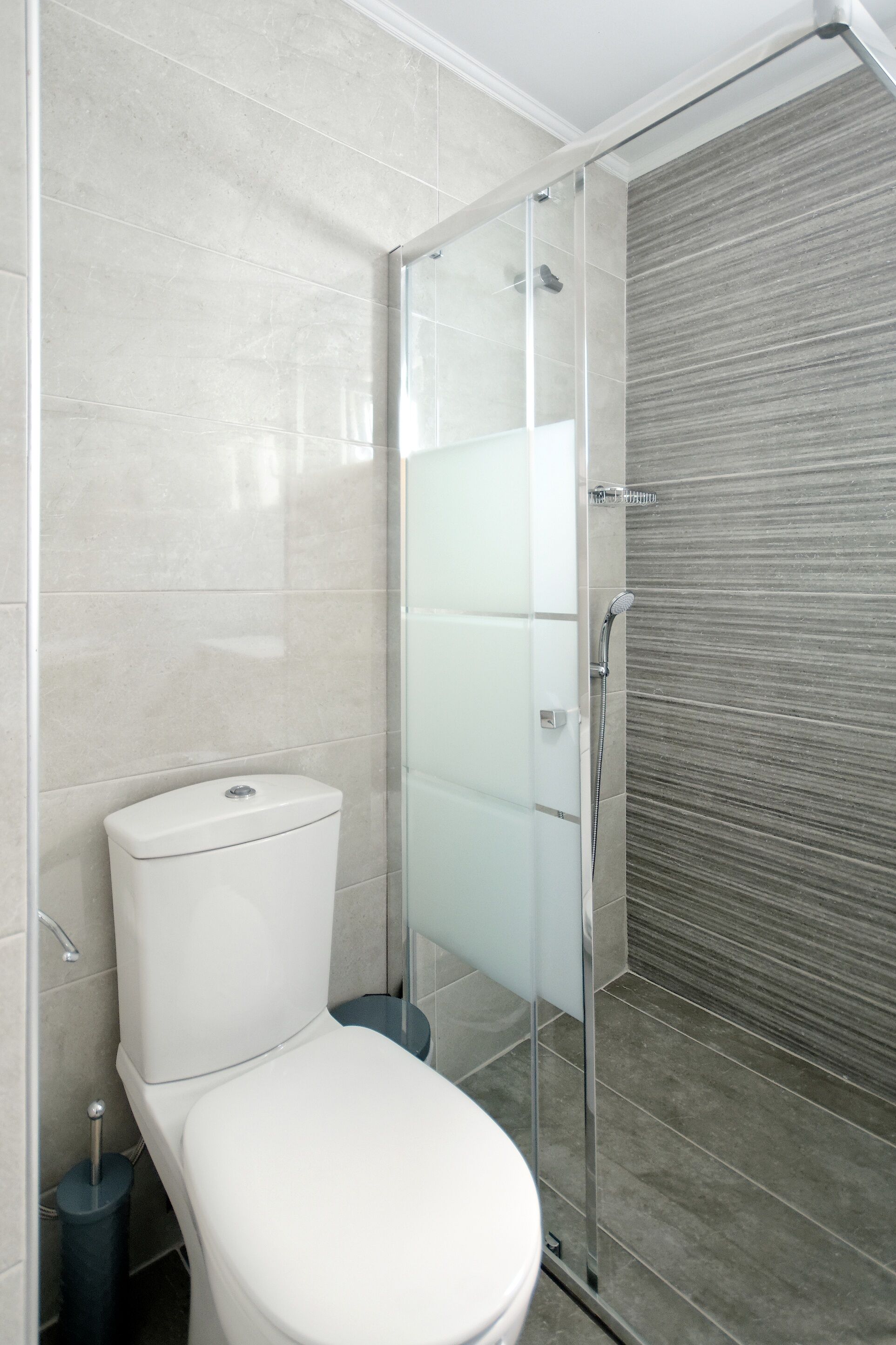 A modern bathroom with a glass-enclosed shower, a white toilet, and a tiled floor.
