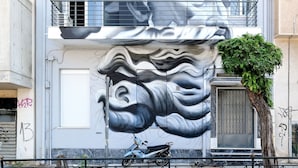 A building with a large mural on the facade, a tree in front, and a parked scooter.