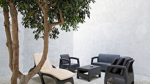 A patio area with a lounge chair, two armchairs, and a small table, all set against a white wall.
