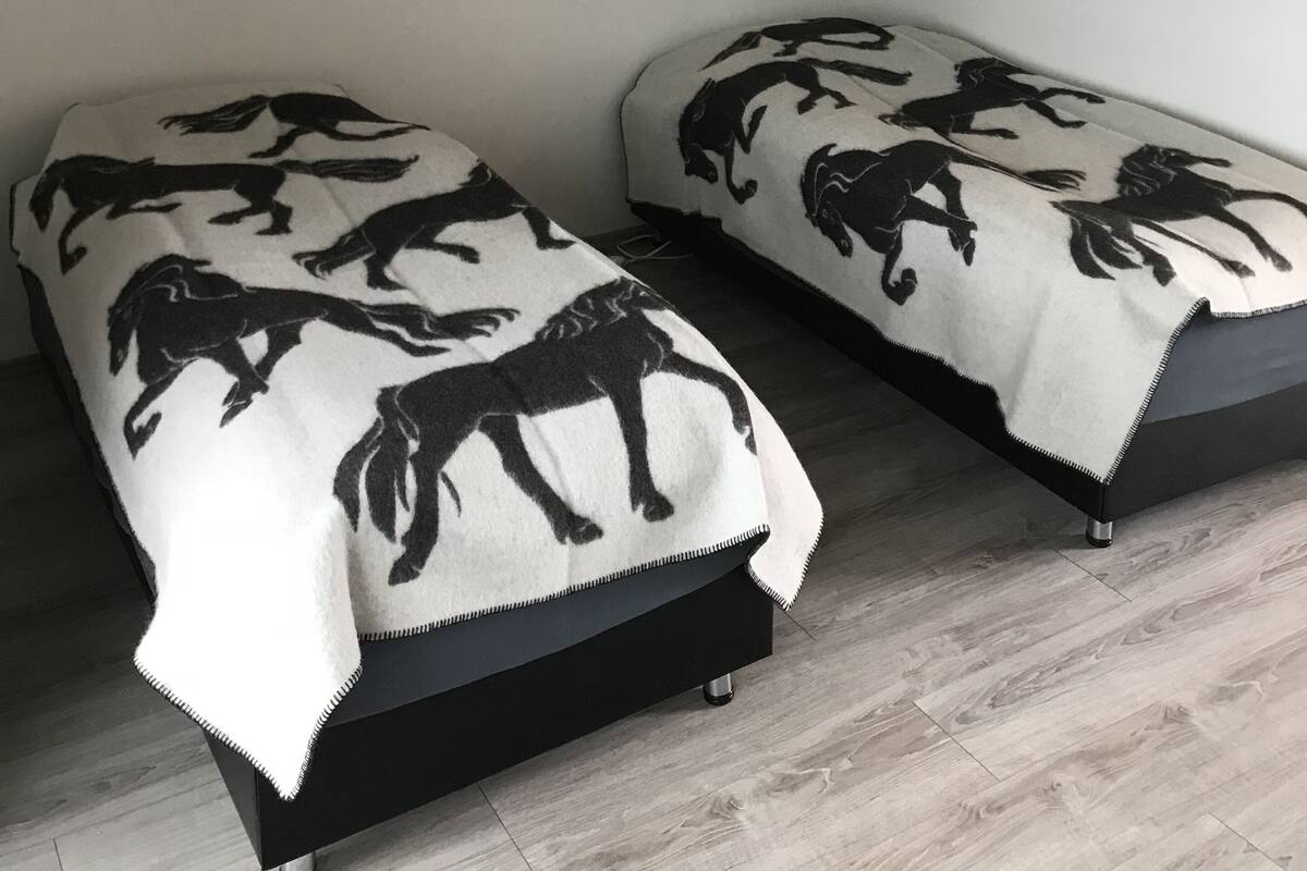 Une chambre avec deux lits, chacun recouvert d’une couverture ornée de silhouettes de chevaux noirs. Un tableau représentant un cheval est accroché au mur.