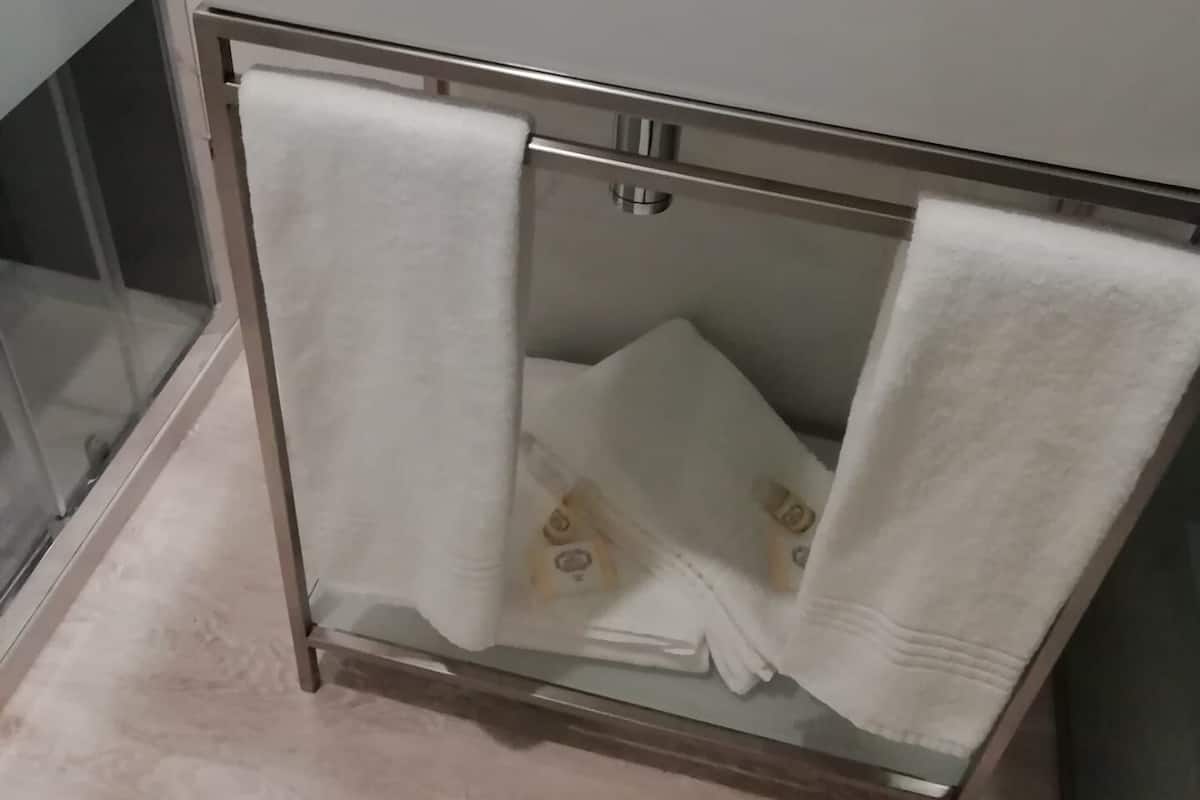A bathroom with a white sink, a glass shower enclosure, and a towel rack with two white towels.