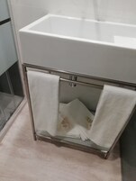 Un baño con un lavabo blanco, cabina de ducha con mampara de cristal y un perchero con dos toallas blancas.