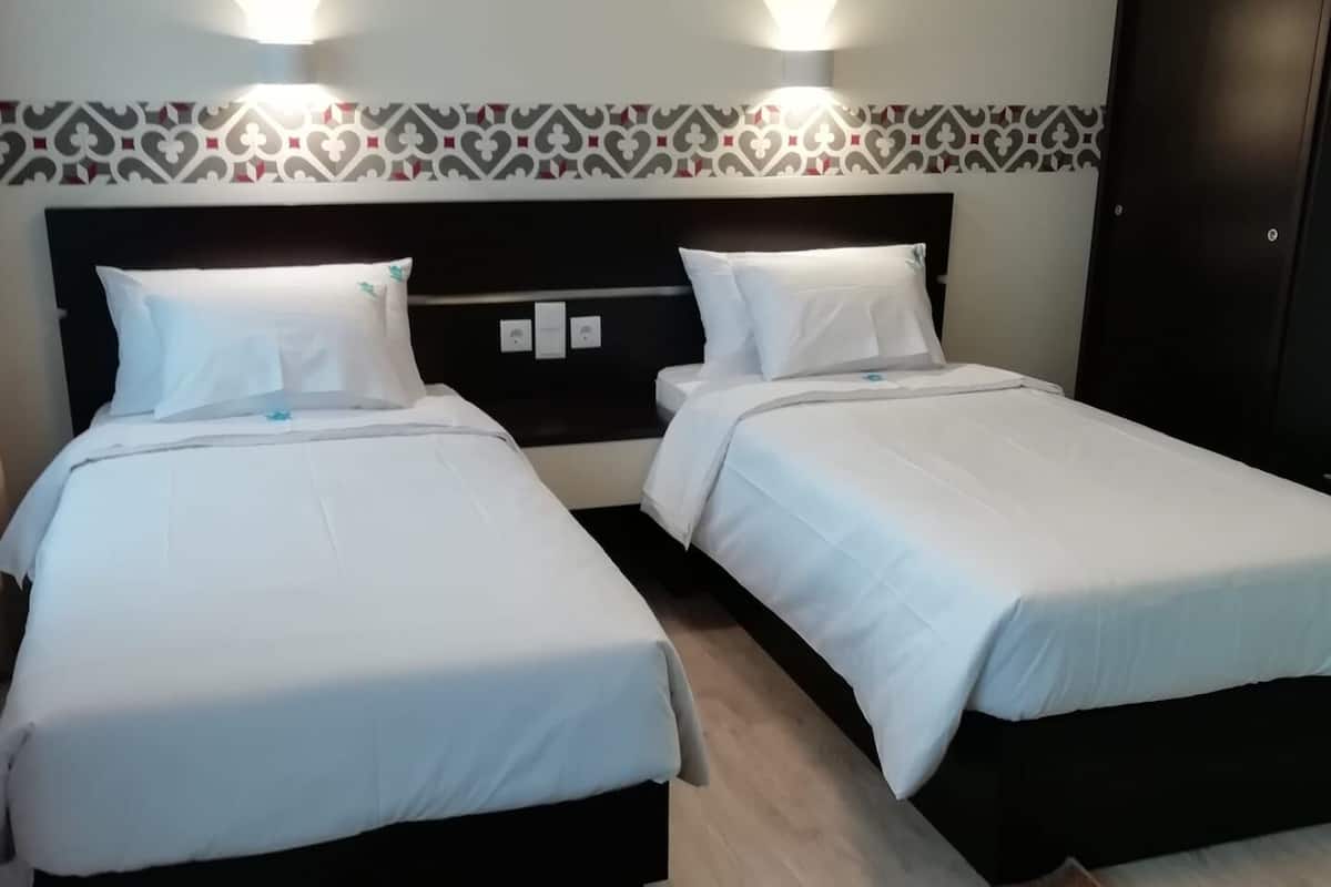 A hotel room with two beds, a patterned headboard, and a brown rug with a fish design.