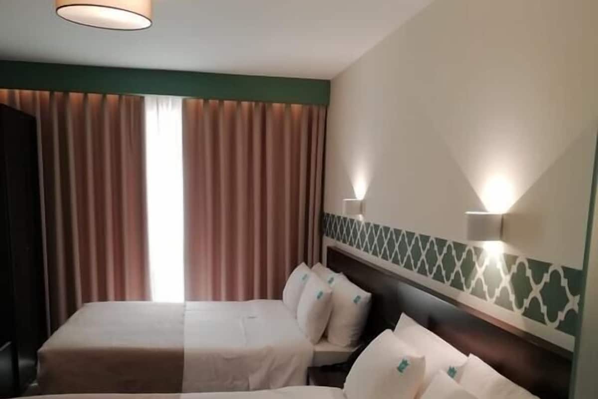 A hotel room with two beds, a window with curtains, and wall-mounted lights.