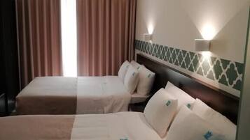 Hotellihuone, jossa on kaksi sänkyä, ikkuna, jossa on verhot, ja seinään kiinnitetyt valaisimet.