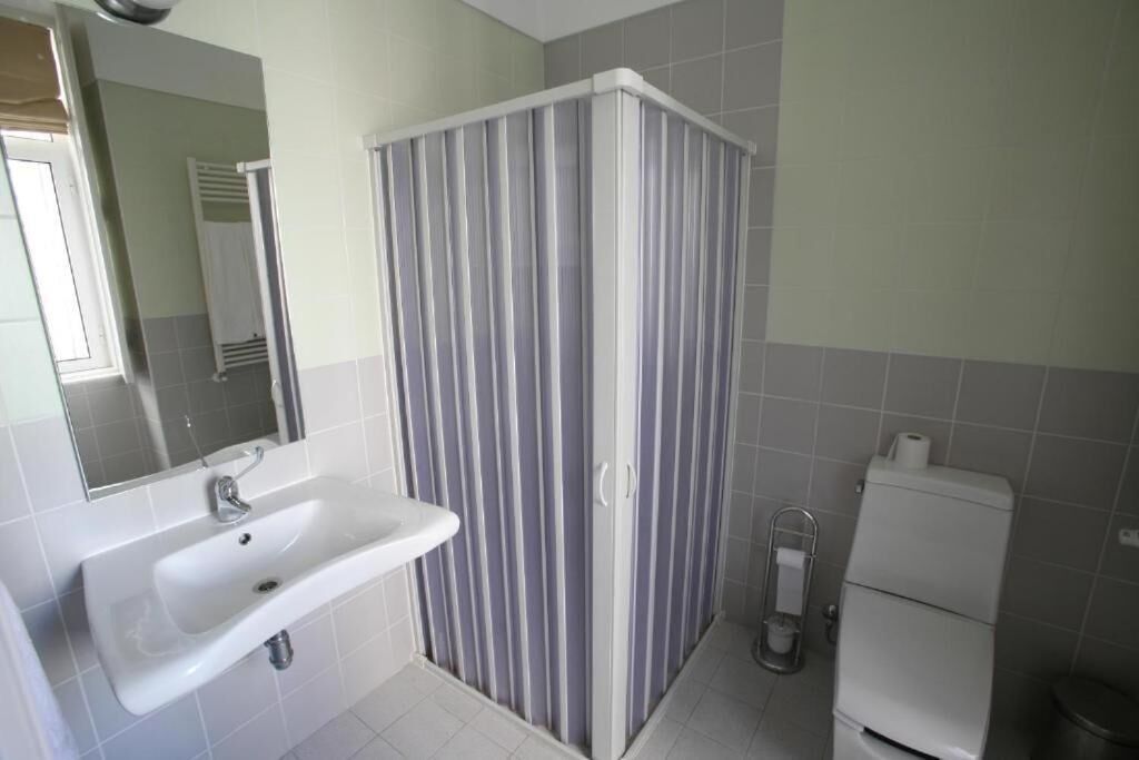 A bathroom with a white sink, a mirror, a striped shower curtain, and a toilet.