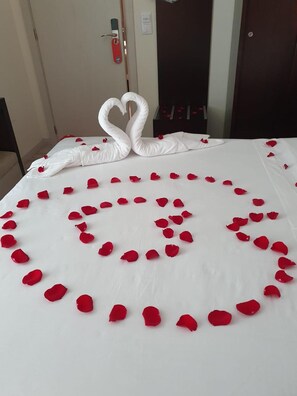 A bed with a white sheet and red rose petals arranged in a heart shape. - Primavera (Amadora)