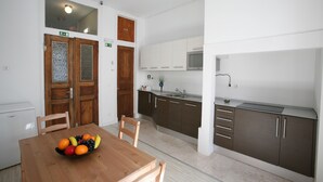 A modern kitchen with dark cabinets, a microwave, and a sink. There is a wooden dining table with chairs and a bowl of fruit. - Primavera (Amadora)