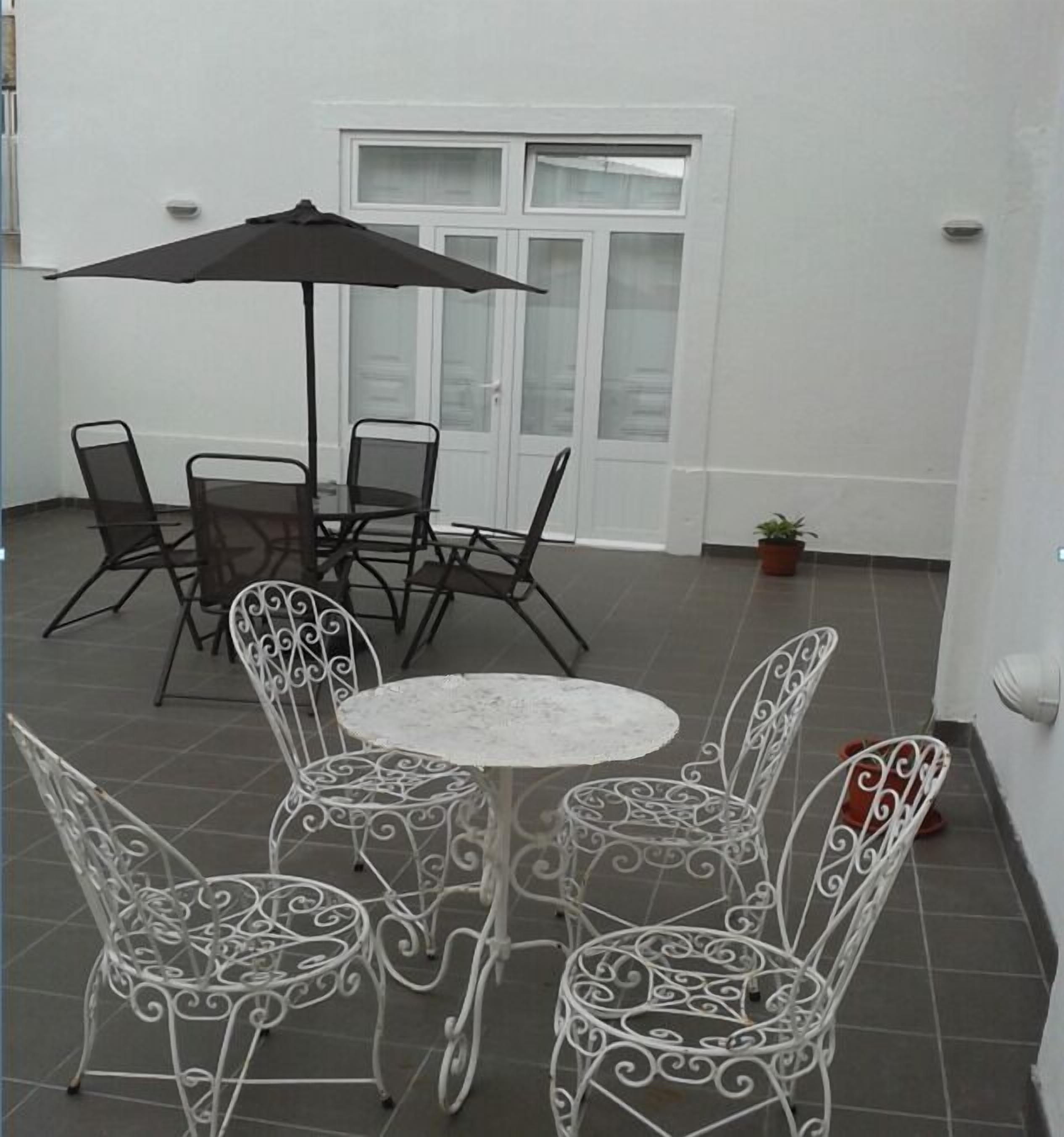 Een terras met een ronde tafel, vier stoelen, een grote parasol en een bloempot.