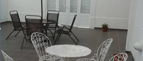 Een terras met een ronde tafel, vier stoelen, een grote parasol en een bloempot.