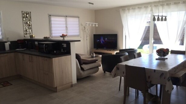 Una cocina moderna con comedor, televisor de pantalla plana y un amplio ventanal con cortinas.
