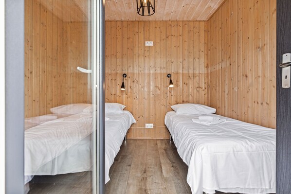 A room with wooden walls and two beds with white bedding. There are two wall-mounted lights and a power outlet on the wall. - Topcamp Onsakervika - Tyrifjorden (Hole)