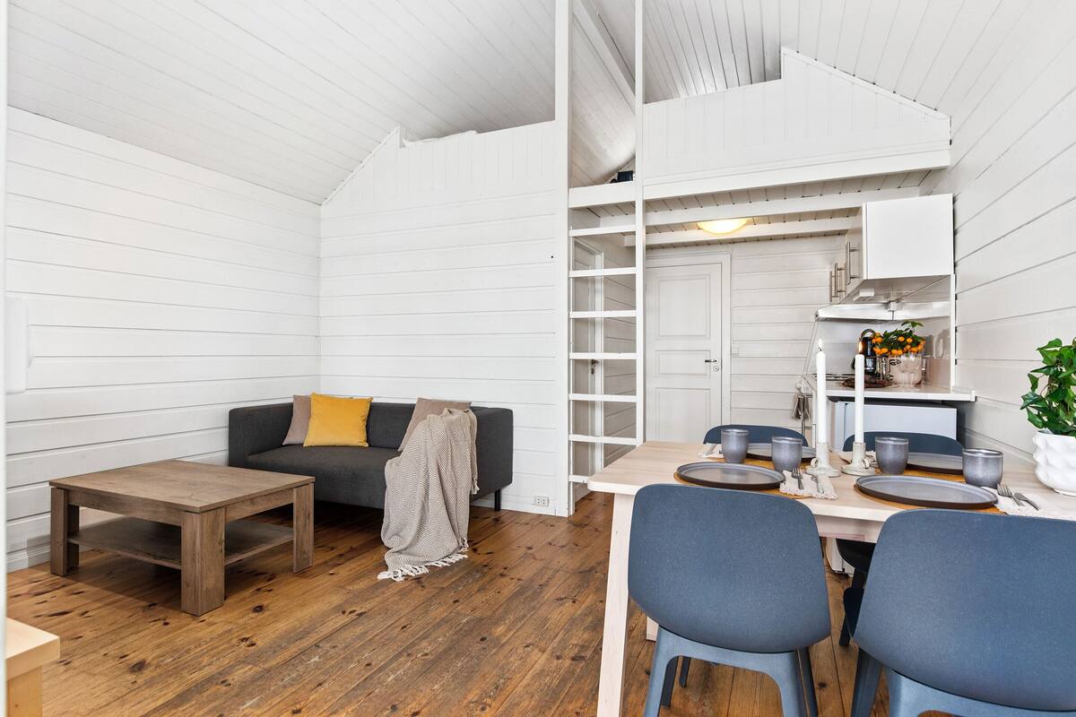 Een gezellig, compact leefruimte met een bank, een klein houten tafeltje, en een eethoek met stoelen en een tafel gedekt voor twee personen.