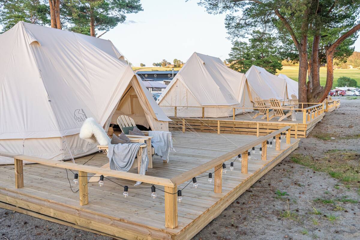 Een rij witte tenten met houten terrassen en stoelen, verbonden door een houten looppad.