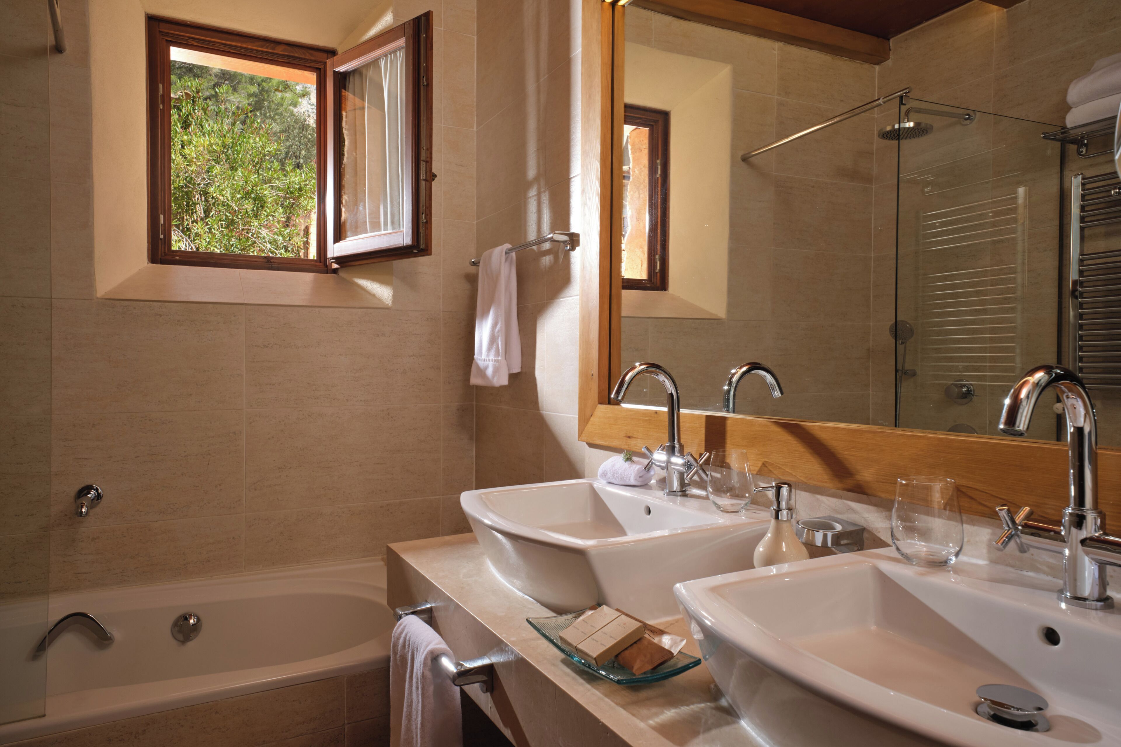 A bathroom with two sinks, a bathtub, and a window with an open shutter.