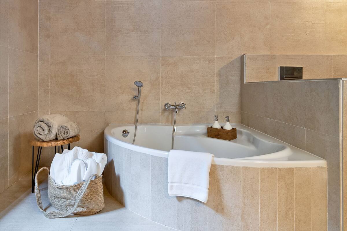 A modern bathroom with a freestanding bathtub, a wooden stool with towels, and a woven basket.