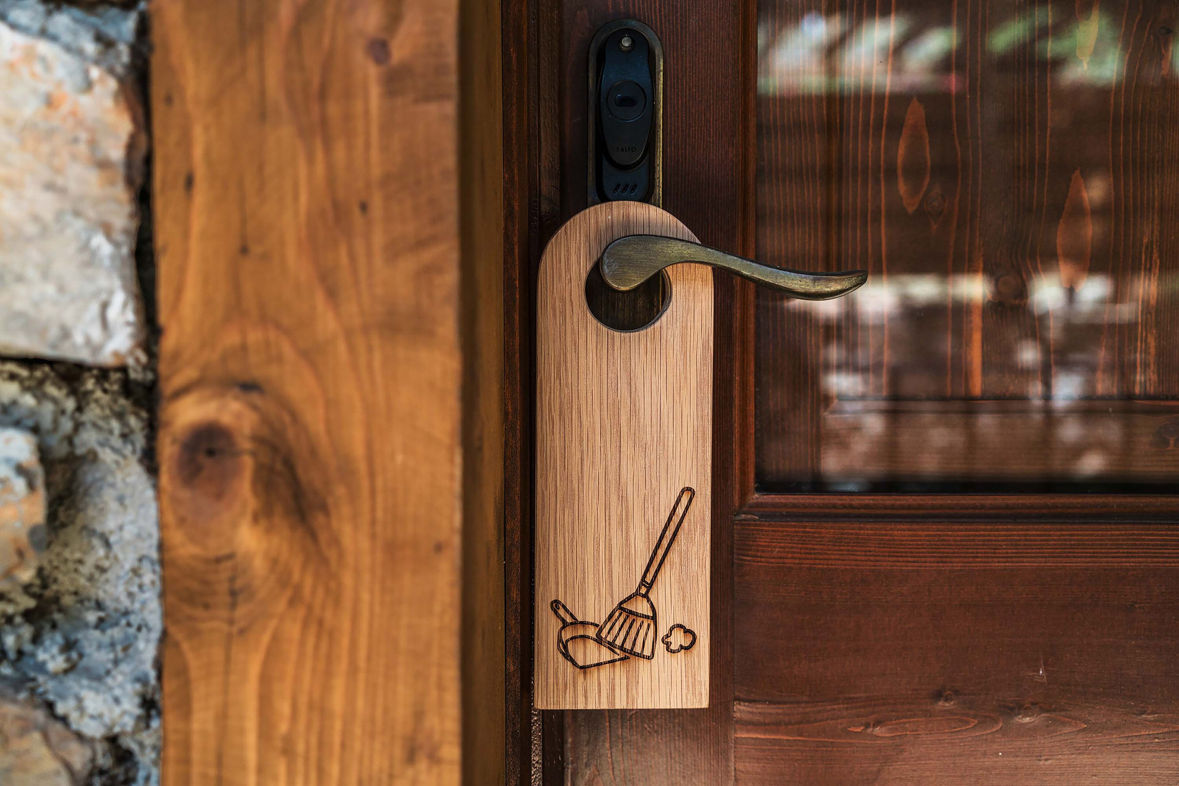 Een houten deur met een metalen handgreep en een houten plaatje met een ontwerp van een bezem en een sopborstel.